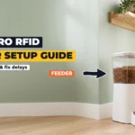 White automatic pet feeder with a full food hopper beside a tabby cat wearing a collar with an RFID tag, against a sage green wall